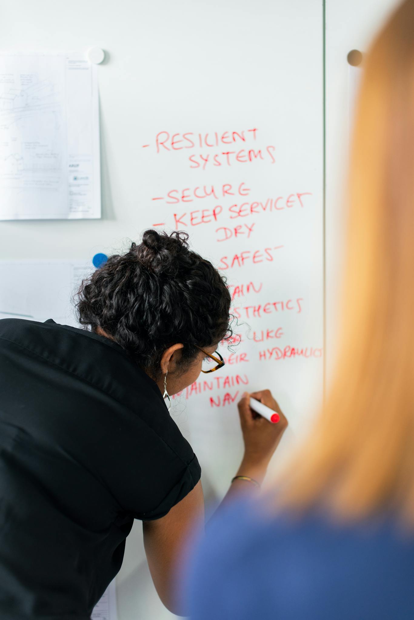 Home Female engineer writing strategy on a whiteboard during a business meeting.