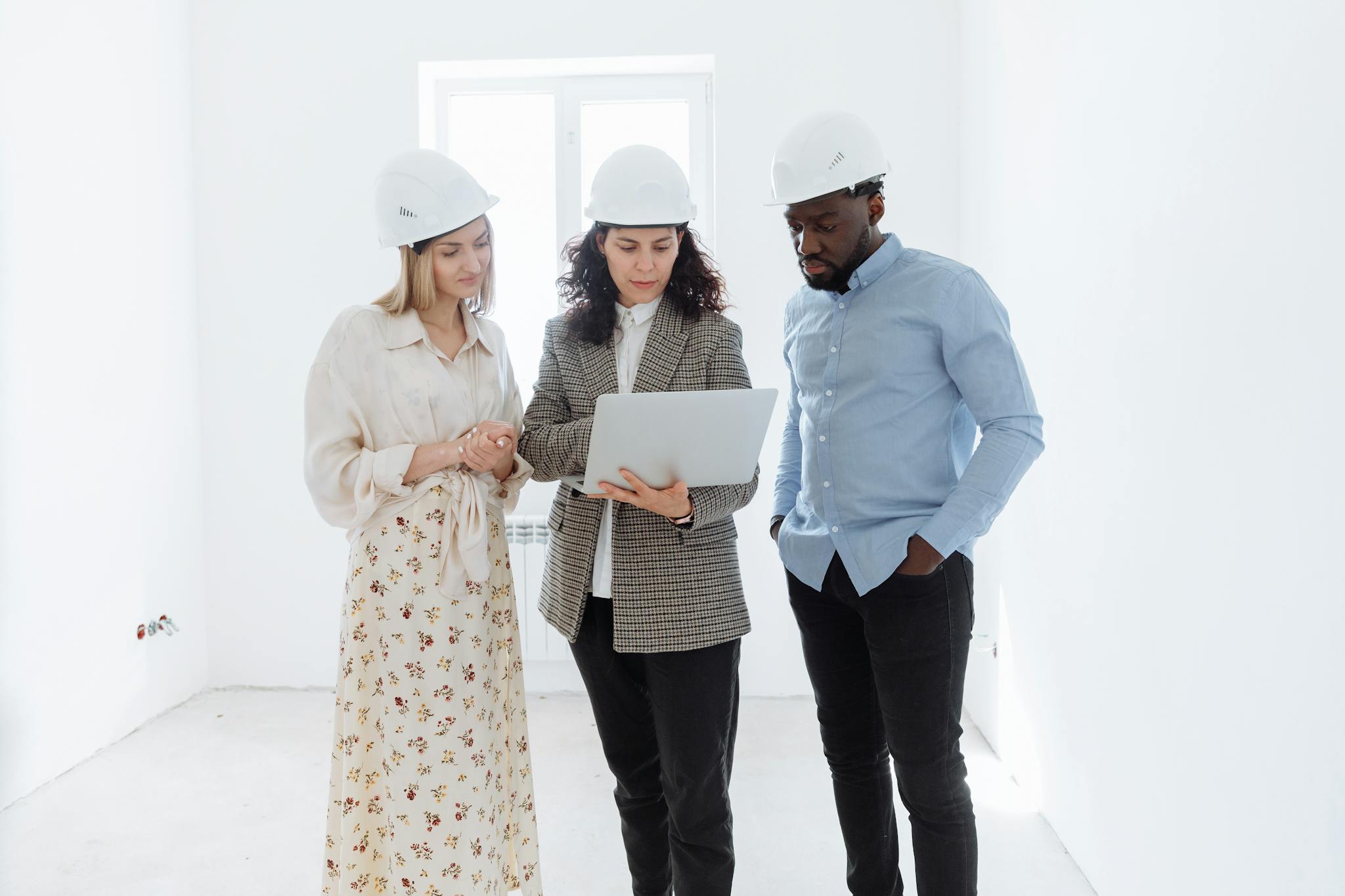 Gallery Three professionals in hard hats examining floor plans on a laptop indoors.