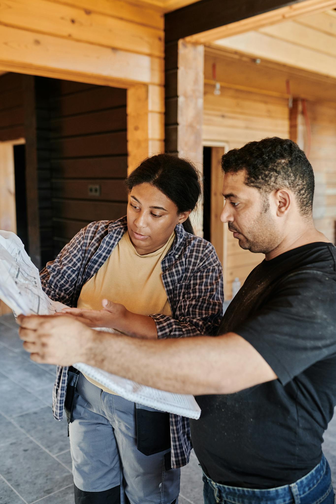 Services Two construction professionals examining blueprints in a wooden building interior.